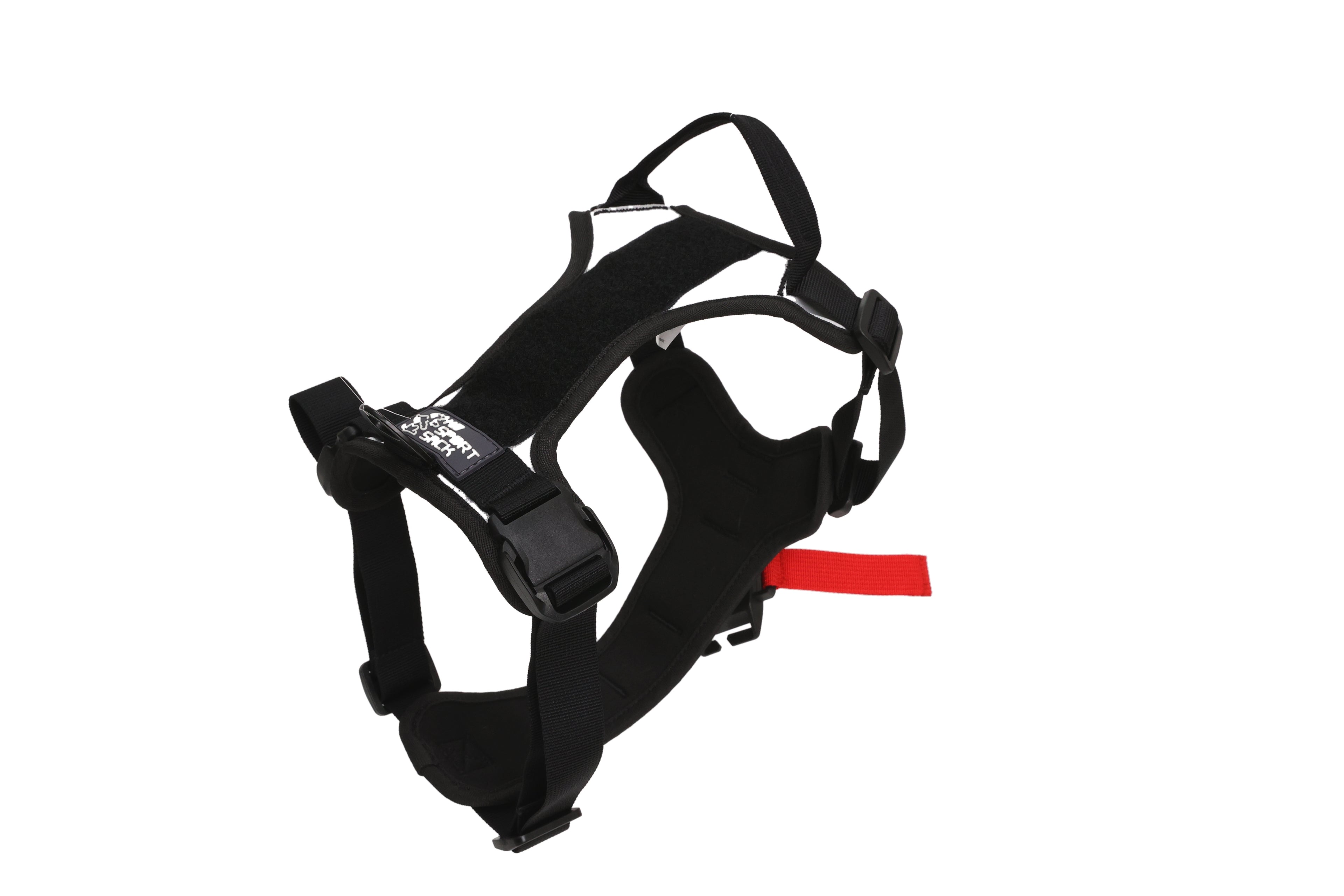 A black dog harness with adjustable straps, plastic buckles, and a small red pull tag for the fidlock system, shown on a plain white background.